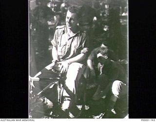 THE SOLOMON ISLANDS, 1945-05. AN AUSTRALIAN SOLDIER RELAXES WITH A BICYCLE WHILE HIS MATES LOOK ON AT NORTH BOUGAINVILLE. (RNZAF OFFICIAL PHOTOGRAPH.)
