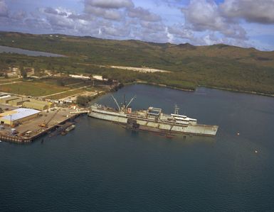 An elevated starboard view of the submarine tender USS PROTEUS (AS 19) moored at Polaris Point, with submarines positioned alongside