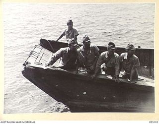 AT SEA, OFF BUIN, BOUGAINVILLE, 1945-08-20. THE REMAINDER OF JAPANESE SURRENDER ENVOY PARTY ON A BARGE LISTENING AS PROGRESS NEWS IS GIVEN OUT BY AN AUSTRALIAN INTERPRETER, DURING SURRENDER ..