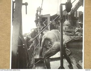 LAE, NEW GUINEA. 1944-06-14/02. CREW MEMBERS OF THE AK94, A VESSEL OF THE 12TH WATER TRANSPORT OPERATING COMPANY, WASHING THEIR SHIP DOWN IN PREPARATION FOR A NEW LOAD OF CARGO FOR MADANG