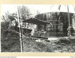 MILNE BAY, PAPUA, NEW GUINEA. 1944-04-03. A BULLDOZER PUSHING SOIL TO FORM A 'BUND', A PROTECTIVE WALL IN CASE OF LEAKAGE, AROUND A 500,000 GALLON OIL TANK AT THE 2ND BULK PETROLEUM STORAGE COMPANY