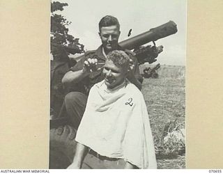 DALLMAN RIVER, NEW GUINEA, 1944-02-23. VX36006 GUNNER R. RYLEY (1), GIVES A HAIRCUT TO ANOTHER MEMBER OF THE 2/14TH FIELD REGIMENT, VX52963 GUNNER E.W. HILL (2), ALONGSIDE A 25-POUNDER GUN