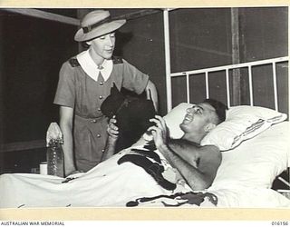 NEW GUINEA. 1943-11-19. LYING IN BED AT AN AUSTRALIAN FIELD HOSPITAL PTE. HAROLD HERMAN, THE HOSPITAL'S "CHEERIEST PATIENT", SHOWS A MEMBER OF THE AUSTRALIAN ARMY MEDICAL WOMEN'S SERVICE (AAMWS), ..