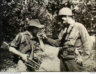 YUAT RIVER, YAGOMAI, NEW GUINEA. 1944-02-10. PRIVATE KEITH WALLER (1) AN AUSTRALIAN BREN GUNNER RECEIVES A CIGARETTE AND LIGHT FROM PRIVATE FIRST CLASS ARCHIE NORMAN, OF TEXAS, AFTER THE LINK UP OF ..