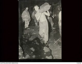 KIRIWINA, TROBRIAND ISLANDS, PAPUA. C. 1943-12. SERGEANT R. E. HENRY OF NAREMBEEN, NSW, CARRYING BAG OF MAIL THROUGH MUD AND RAIN
