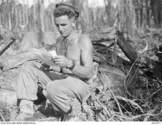 BOUGAINVILLE. 1945-05-22. PRIVATE H. WASHUSEN, 24 INFANTRY BATTALION, STOPS DIGGING TO READ HIS MAIL. HE IS SEATED ON THE STUMP OF A TREE DESTROYED BY ROYAL NEW ZEALAND AIR FORCE AIRCRAFT AT EGAN'S ..