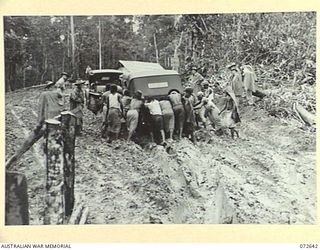 FINSCHHAFEN AREA, NEW GUINEA. 1944-04-25. NATIVES FROM THE SONG RIVER NATIVE COMPOUND, AUSTRALIAN NEW GUINEA ADMINISTRATIVE UNIT, PUSHING A JEEP CONTAINING MEMBERS OF THE OFFICIAL PARTY ..
