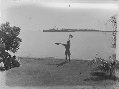 [A man in uniform with flag signals directing a ship]