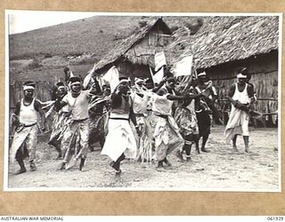 KILA KILA, PAPUA, NEW GUINEA. 1943-12-25. KEREMA BOYS EXECUTING A DANCE AT THE AUSTRALIAN AND NEW GUINEA ADMINISTRATION UNIT NATIVE LABOUR CAMP. THE DANCERS WEAR LONG TRAILS OF GRASS AND FLOWERS, ..