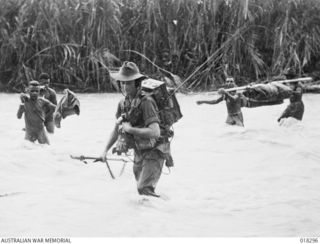 Aitape Sector, New Guinea. 1945-03-27. Australian troops and native supply trains mingle as they cross one of the countless streams to be negotiated on the advance along the coast towards But