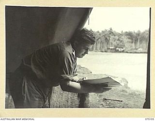 MILILAT, NEW GUINEA. 1944-08-07. NX133264 MAJOR D.R. ROBERTSON, DEPUTY ADJUTANT AND QUARTERMASTER GENERAL, HEADQUARTERS, 5TH DIVISION, READING IN HIS TENT