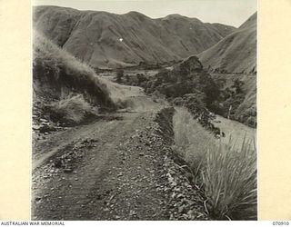 WAU - LAE ROAD, NEW GUINEA, 1944-02-26. THE ROAD VIEWED TOWARDS SUNSHINE SHOWING THE ROAD CUT IN THE WATUT VALLEY WITH A SMALL LANDSLIDE TO THE LEFT OF THE ROAD. THE ROAD IS MAINTAIND BY THE 1ST ..