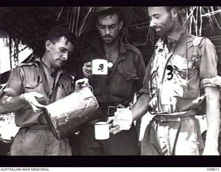 DUMPU, NEW GUINEA. 1943-10-15. VX67928 CORPORAL (CPL) J. KNUCKEY (1) OF THE SALVATION ARMY RED SHIELD SERVICES AT THE SALVATION ARMY HUT POURING A CUP OF COFFEE FOR SX4134 PRIVATE R. W. FOGG (2), ..