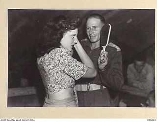 TOROKINA, BOUGAINVILLE. 1945-04-16. LIEUTENANT N.L. GRIMM, AMENITIES OFFICER, 29 INFANTRY BRIGADE (2), AT HEADQUARTERS 29 INFANTRY BRIGADE, HELPING ELVA QUIN (1), A MEMBER OF THE BOB DYER CONCERT ..