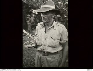 New Guinea. 1943-11-20. TX3539 Private R. W. Hawkins, 2/12th Australian Infantry Battalion, AIF, displaying an ash tray he made, in his spare time, from cartridge cases