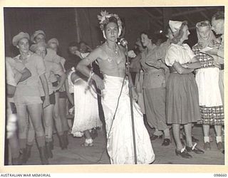 LAE, NEW GUINEA. 1945-11-08. CORPORAL A. MILGATE, THE ANNOUNCER AT THE FANCY DRESS PARTY HELD BY MEMBERS OF AUSTRALIAN WOMEN'S ARMY SERVICE BARRACKS TO FAREWELL CAPTAIN M.W. HORNSBY AND CAPTAIN ..