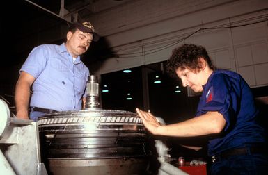 Aviation Machinist's Mate 1ST Class (AD1) Tamara Kimm and AD1 Gary Simmons repair a T56-A14 turbine assembly at the Aircraft Intermediate Maintenance Department