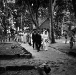 Bride and groom followed by attendants and well-wishers stroll the village paths