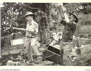 MADANG, NEW GUINEA. 1944-04-28. 5TH DIVISION OFFICERS EXAMINING A RANGE FINDER AND BINOCULARS AMONG A DUMP OF ABANDONED JAPANESE EQUIPMENT AT MATUPI. THE BINOCULARS ARE DESIGNED TO ASSIST AIRCRAFT ..