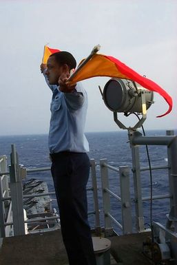 Signalman Third Class (SM3) Young makes flag signals on board USS SAIPAN (LHA 2) during a training exercise