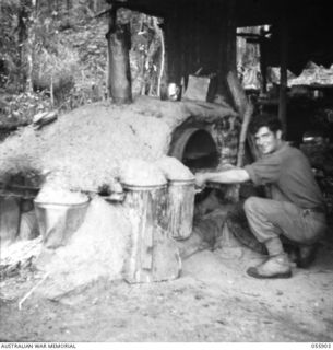 SKINDEWAI, NEW GUINEA, 1943-08-13. SX18865 PRIVATE CHEETHAM, A COOK OF THE 2/6TH BATTALION. NOTE THE OVEN AS AN EXAMPLE OF AUSTRALIAN INGENUITY