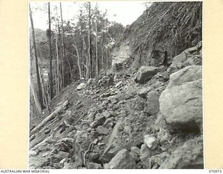 ZENAG, NEW GUINEA, 1944-02-28. IN ORDER TO WIDEN THE EXISTING TRACK, THE ROCK FACE HAS BEEN BLASTED, BRINGING DOWN EARTH WHICH WILL BE CLEARED BY BULLDOZERS