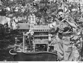 SCARLET BEACH AREA, NEW GUINEA. 1943-12-21. NX114310 STAFF SERGEANT J. E. ROGERS (1) AND QX4865 WARRANT OFFICER I, C. W. KINGSTON (2) OPERATING A MACHINE WHICH WAS BUILT BY THE UNIT AT THE 1ST ..