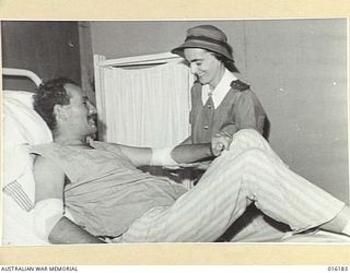 NEW GUINEA. 1943-11-22. AT AN AUSTRALIAN FIELD HOSPITAL SISTER C. CLARKE BANDAGES THE ARM OF AN AUSTRALIAN SOLDIER LYING IN BED