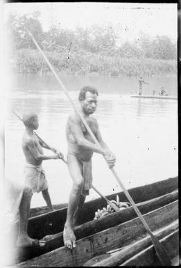 Man and a boy standing in a canoe leaning against long poles, Ramu River, New Guinea, 1935 / Sarah Chinnery