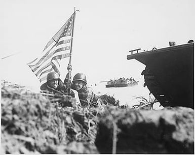 First flag on Guam on boat hook mast. Two U.S. officers plant the American flag on Guam eight minutes after U.S. Marines and Army assault troops landed on the Central Pacific island on July 20, 1944.