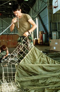 A1C Donald Popp, 8th Mobile Aerial Port Squadron, repairs suspension lines on parachute prior to attaching packages to be delivered during Christmas Drop. The annual airdrop is a humanitarian effort providing aid to needy islanders throughout Micronesia during the holiday season