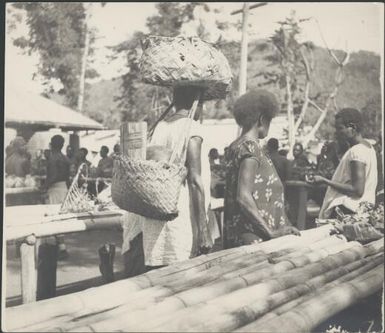 Heavily laden woman, passing between trestle tables, Boong market, Rabaul, New Guinea, ca. 1936 / Sarah Chinnery