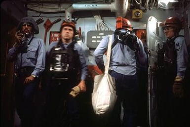 A member of a repair party uses a sound-powered phone to relay information while members of a firefightin team, wearing oxygen breathing apparatuses, stand ready for a drill aboard the amphibious assault ship USS GUAM (LPH 9)