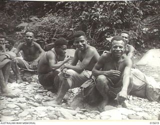 1943-08-30. NEW GUINEA. NATIVE CARRIERS AT A LAUNCH HOUR HALT AT THE FOOT OF MOUNT TAMBU. (NEGATIVE BY H. DICK)