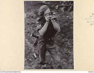 MAMAGOTA AREA, BOUGAINVILLE. 1945-07-22. BOMBARDIER V.H. SMITH, 3 SURVEY BATTERY, ROYAL AUSTRALIAN ARTILLERY, MEASURING HEIGHTS WITH AN ABNEY LEVEL FOR RECORDINGS; THE RECORDINGS ASSIST ARTILLERY ..