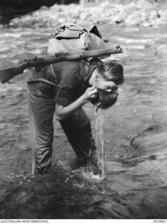 SX18513 TROOPER WILLIAM FRANK BYRNE, 2/8 COMMANDO SQUADRON STOPS FOR A DRINK FROM HIS BERET WHILE CROSSING THE HONGORAI RIVER ON HIS WAY TO SQUADRON HEADQUARTERS AT MOROKAIMORO