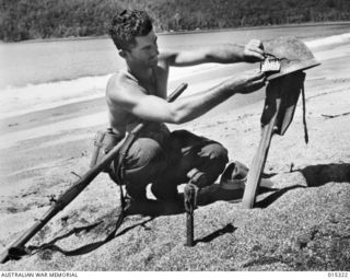 Allied capture of Mubo. Private (Pte) Dennis Buzza of Brisbane, Qld, places a Japanese officer's identification emblem on his grave after the officer had been killed in a skirmish on Nassau Bay ..