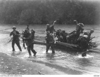 ORO BAY AREA, NEW GUINEA. 1942-11-12. INFANTRYMEN OF THE 128TH REGIMENT, 32ND UNITED STATES DIVISION CROSSING A FLOODED CREEK BY NATIVE CANOES IN A TORRENTIAL DOWNPOUR DURING THEIR ADVANCE ON BUNA