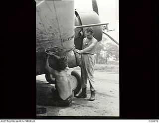 NADZAB, NEW GUINEA. C. 1944-02. LEADING AIRCRAFTMAN (LAC) K. E. WILLIAMS, KOGARAH, NSW (BACK TO CAMERA), PLACES A PARACHUTE CANISTER ON BOMB RACKS OF A WIRRAWAY AIRCRAFT OF NO. 4 (ARMY COOPERATION) ..