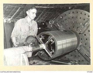 LABU, NEW GUINEA. 1944-10-03. CRAFTSMAN J.L. EASON TURNING UP ONE OF THE 14 INCH DIAMETER PISTONS OF THE VESSEL THE "FRANCES PEAT" ON A LARGE LATHE IN THE WORKSHOP OF THE 1ST WATERCRAFT WORKSHOPS. ..