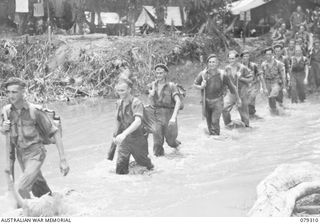 BOUGAINVILLE ISLAND. 1945-03-01. PERSONNEL OF THE 61ST INFANTRY BATTALION WADING THROUGH A SECTION OF THE MOSIGETTA ROAD WHICH HAS BEEN FLOODED BY THE OVERFLOWING HUPAI RIVER. IDENTIFIED PERSONNEL ..