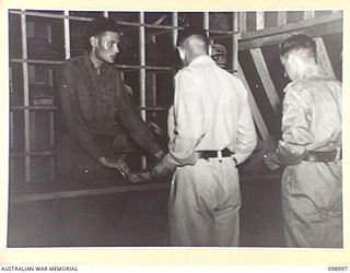 LAE, NEW GUINEA, 1945-11-25. PTE W. ZIMMERMAN, AT THE AUSTRALIAN ARMY CANTEENS SERVICE OFFICERS' CLUB CHECKING IN OFFICERS' CAPS AND HATS. THE CLUB IS SITUATED ON THE BANKS OF THE BUSU RIVER