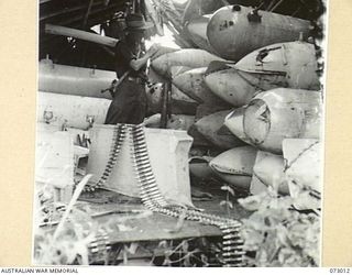 MADANG, NEW GUINEA. 1944-04-26. AN AUSTRALIAN SOLDIER EXAMINES PLYWOOD BELLY TANKS DISCOVERED WITH AMMUNITION SUPPLIES IN A BOMB DAMAGED JAPANESE STORE HOUSE. THE TANKS ARE USED TO PROVIDE ..