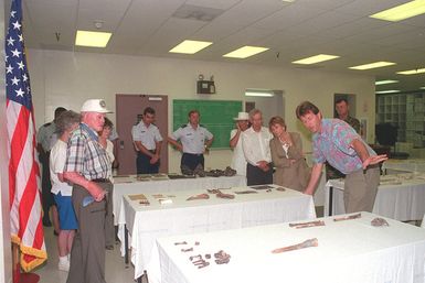 A display of a recent finding of bones by the Army Central Identification Laboratory Hawaii is laid out on white covered tables. A staff member explains them to a small group including Secretary of the Air Force Sheila Widnall and Medal of Honor recipient, Red Erwin. The are here for the 50th anniversary commemoration of World War II