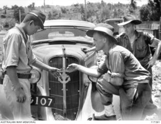 NAURU ISLAND. 1945-09-14. A JAPANESE POW EXPLAINING THE MEANING OF THE JAPANESE NAVY INSIGNIA ON HIS CAR RADIATOR TO PRIVATE TRANSTON, 222ND AUSTRALIAN SUPPLY DEPOT PLATOON