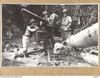 GODOWA, NEW GUINEA. 1943-11-05. AN AUSTRALIAN SOLDIER YARNING WITH MEMBERS OF THE UNITED STATES 102ND COAST ARTILLERY BATTALION WHO ARE MANNING A 50 CALIBRE MACHINE GUN POST ON THE BEACH. LEFT TO ..