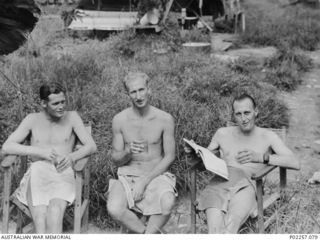 Madang, New Guinea, 1945-08-15. Wearing only towels wrapped around their waists, three officers serving with Headquarters, RAAF Northern Command (NORCOM), relax in easy chairs and enjoy celebratory ..