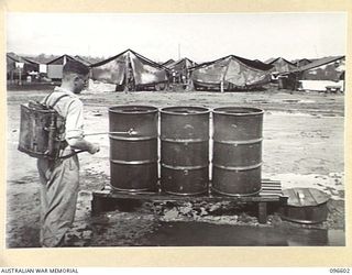 CAPE WOM, WEWAK AREA, NEW GUINEA. 1945-09-15. PRIVATE H. STILLMAN, HYGIENE PLATOON, HEADQUARTERS 6 DIVISION, SPRAYING ANTI-MALARIA FLUID AROUND THE KITCHEN REFUSE TINS. HE ALSO SPRAYS ANY WATER ..