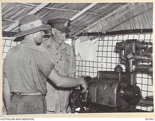 BOUGAINVILLE. 1945-05-10. CAPTAIN C.T. COLQUOHN, 42 LANDING CRAFT COMPANY (1), SHOWING LIEUTENANT GENERAL V.A.H. STURDEE, GENERAL OFFICER COMMANDING FIRST ARMY (2), THE WORKING OF A JAPANESE LATHE ..