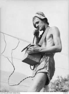 PORT MORESBY, PAPUA. 1942-07. A BRONZED AUSTRALIAN SIGNALLER TESTS THE LINE TO AN ARMY OUTPOST IN THE NEW GUINEA BUSH